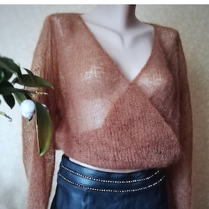 Può includere: Un maglione a maniche lunghe trasparente color rame con scollo a V e design a portafoglio sul davanti. Il capo presenta una trama a maglia larga e aperta ed è abbinato a una gonna in pelle nera decorata con una fila di piccole borchie argentate.