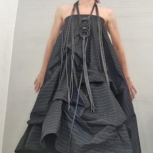 May include: A black and white striped maxi dress with a black leather necklace featuring three large rings. The dress has a layered, ruffled design and is paired with white platform sandals with black accents.