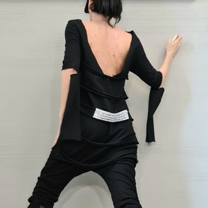 Könnte beinhalten: Ein schwarzes Outfit mit tiefem Rücken, bestehend aus einem langärmeligen Oberteil mit gebundenem Detail und einer schwarzen Hose. Das Outfit wird mit schwarzen Plateau-Stiefeln mit weißen Farbspritzern kombiniert.