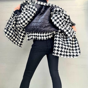 May include: A black and white houndstooth jacket with a black quilted back panel, paired with solid black leggings and black block-heeled ankle boots featuring small attached pouches on the outer sides of the ankles and buckle strap details.