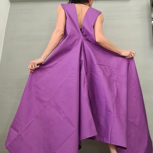 Może przedstawiać: Fioletowa sukienka bez rękawów z głębokim dekoltem w kształcie litery V i falującą spódnicą. Sukienka jest asymetryczna, z jedną stroną dłuższą niż druga. Modelka nosi białe platformy z czarno-białymi wzorzystymi podeszwami.