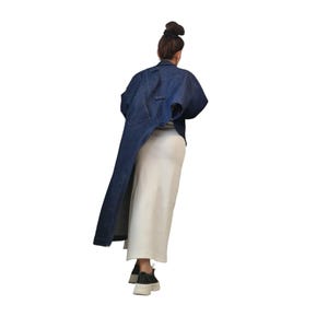 May include: A dark blue denim jacket with a unique asymmetrical design, featuring a long, flowing panel on one side. The jacket is paired with a cream-colored skirt and black sneakers, creating a modern, stylish ensemble.