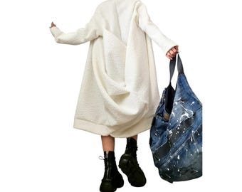 May include: A long-sleeved, off-white textured fleece coat with a loose, draped silhouette. The coat is paired with black platform boots and a large, dark blue denim hobo bag featuring white paint splatter details and black leather accents.