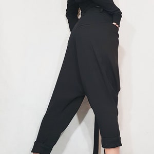 May include: Black, long-sleeved top with an asymmetrical neckline and black, loose-fitting pants. The pants have a unique, draped design. The outfit is paired with black ankle boots with a chunky heel and a zipper detail.