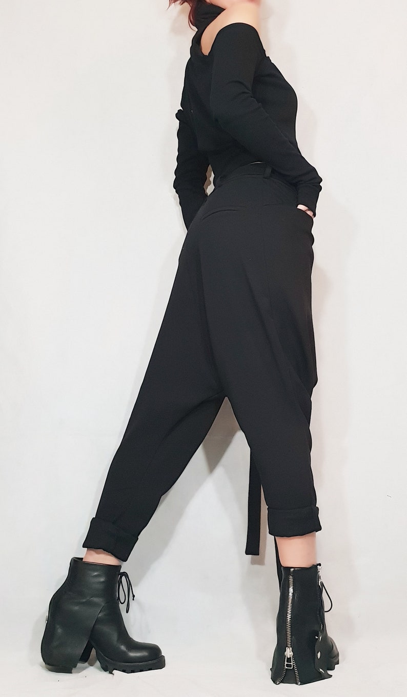 May include: Black, long-sleeved top with an asymmetrical neckline and black, loose-fitting pants. The pants have a unique, draped design. The outfit is paired with black ankle boots with a chunky heel and a zipper detail.