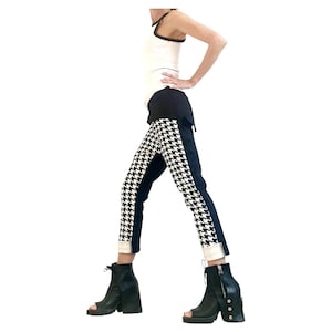 May include: A white tank top with black trim, paired with black and white houndstooth pants. The pants have a black side panel and are cuffed at the ankle. Black open-toe boots with block heels complete the outfit.