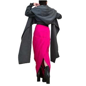 Könnte beinhalten: Eine dunkel anthrazitfarbene Kapuzenjacke mit langen, weiten Ärmeln kombiniert mit einem leuchtend fuchsiafarbenen Maxirock mit Wickeloptik auf der Vorderseite und sichtbaren Nähten. Das Outfit wird durch schwarze Stiefeletten mit Blockabsatz ergänzt.