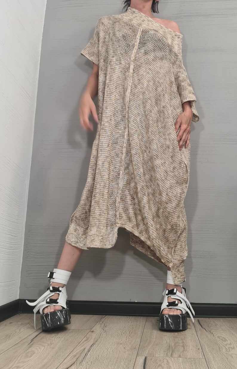 May include: A loose-fitting, beige and white heathered knit tunic dress with an asymmetrical hemline and short sleeves. The garment is paired with white platform sandals featuring black buckle straps and a black and white marbled sole design.