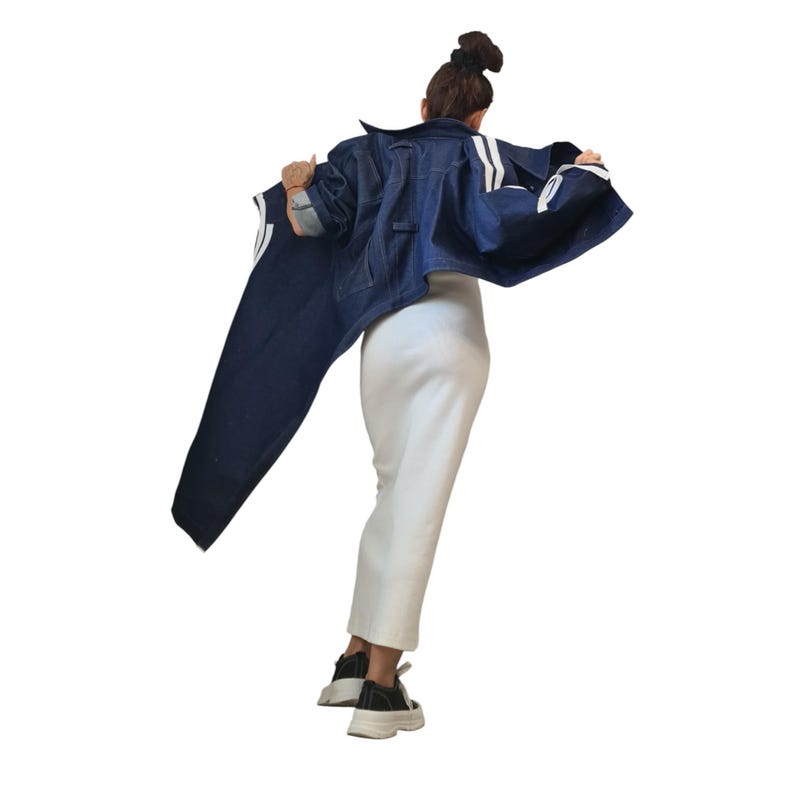 May include: A denim jacket with white stripes on the sleeves and a pair of matching denim pants. The person is wearing a white skirt and black sneakers with white soles. The outfit is set against a white background.
