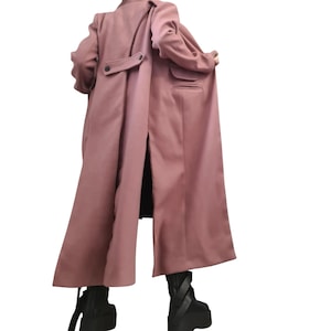 Peut inclure: Un long manteau rose poudré doté d'une fente arrière, d'une patte horizontale au dos avec deux boutons foncés et d'une poche à rabat sur le côté droit. Le manteau présente des manches longues, un col structuré et des bottines à plateforme noires.