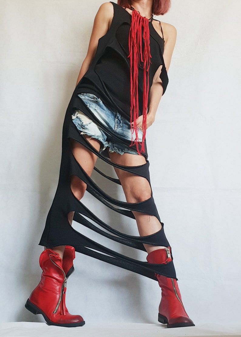 May include: A black, sleeveless dress with a shredded design, paired with denim shorts. The dress features cut-out details and is accessorized with a red fringe necklace. The outfit is completed with red leather ankle boots with zippers.