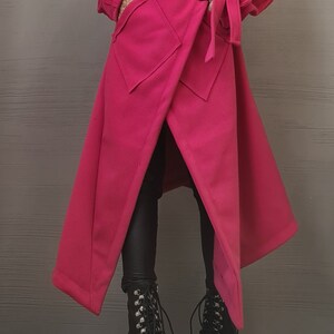 K&ouml;nnte beinhalten: Ein leuchtend fuchsiafarbener Wickelmantel mit breitem Kragen, langen &Auml;rmeln und einem Bindeg&uuml;rtel. Der Mantel hat zwei gro&szlig;e Vordertaschen und einen asymmetrischen Saum. Er wird mit einer schwarzen Leggings und schwarzen Schn&uuml;rstiefeln kombiniert.
