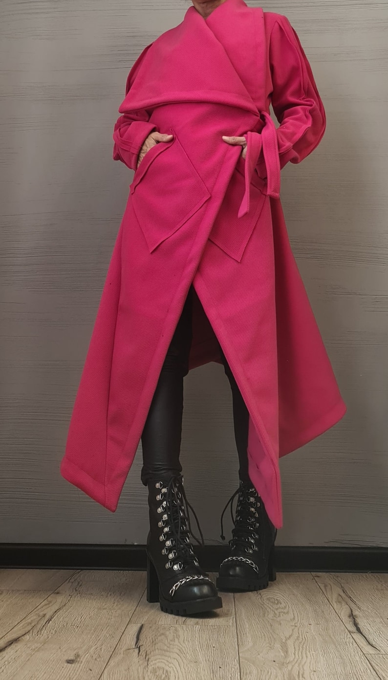 K&ouml;nnte beinhalten: Ein leuchtend fuchsiafarbener Wickelmantel mit breitem Kragen, langen &Auml;rmeln und einem Bindeg&uuml;rtel. Der Mantel hat zwei gro&szlig;e Vordertaschen und einen asymmetrischen Saum. Er wird mit einer schwarzen Leggings und schwarzen Schn&uuml;rstiefeln kombiniert.