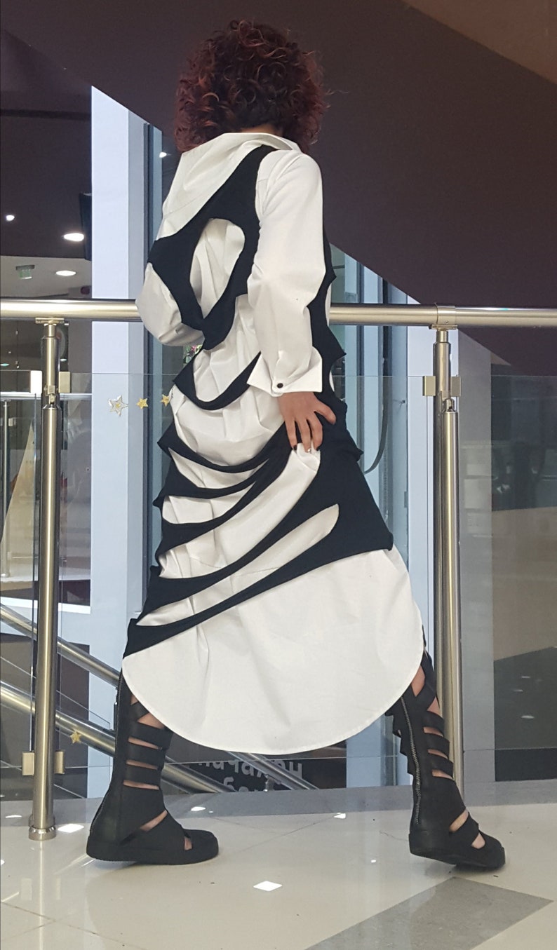 May include: A white shirt with a black, cut-out design, paired with black sandals. The outfit features a unique, layered aesthetic. The model is wearing black sandals.