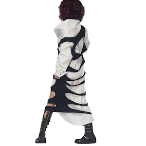 May include: A white long-sleeved shirt with a black overlay featuring cut-out designs. The outfit is paired with black sandals and knee-high gladiator sandals. The overall style is avant-garde and modern.