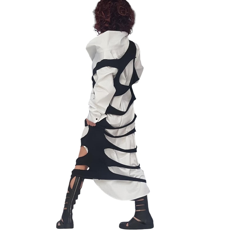 May include: A white long-sleeved shirt with a black overlay featuring cut-out designs. The outfit is paired with black sandals and knee-high gladiator sandals. The overall style is avant-garde and modern.