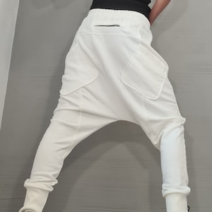 Op de afbeelding: Witte broek met lage kruis met grote zakken en een zwart ritsdetail. De broek wordt gecombineerd met een zwarte tanktop met witte bies en zwart-witte sneakers. De outfit heeft een moderne, stijlvolle uitstraling.