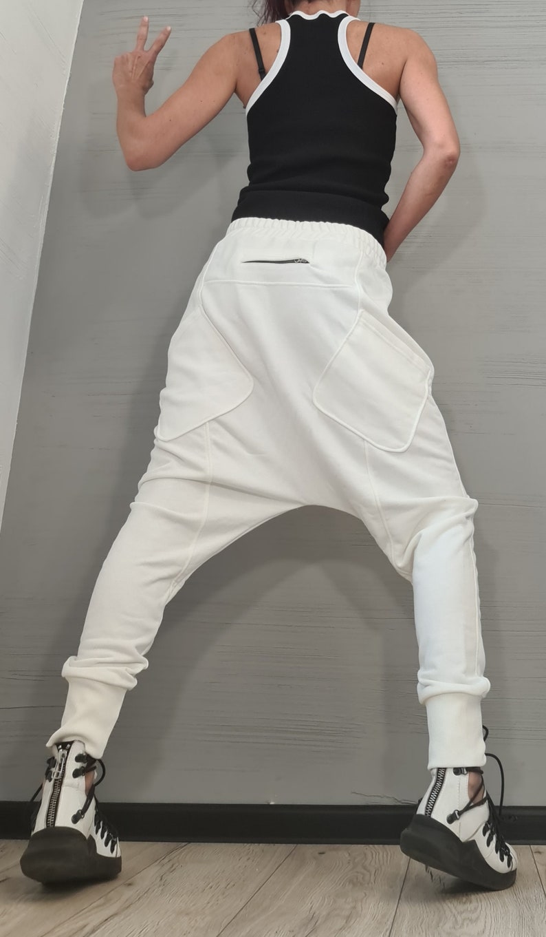 Op de afbeelding: Witte broek met lage kruis met grote zakken en een zwart ritsdetail. De broek wordt gecombineerd met een zwarte tanktop met witte bies en zwart-witte sneakers. De outfit heeft een moderne, stijlvolle uitstraling.
