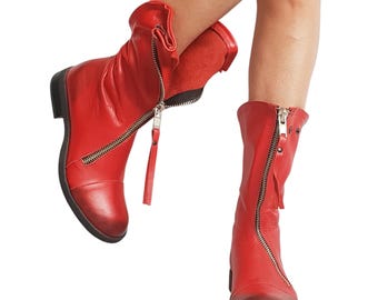 Puede incluir: Botas de cuero rojas con cremallera lateral y punta redondeada. Las botas tienen un tacón bajo y una parte superior doblada. La cremallera se extiende desde la parte superior de la bota hasta el tobillo. Las botas son de color rojo vibrante.