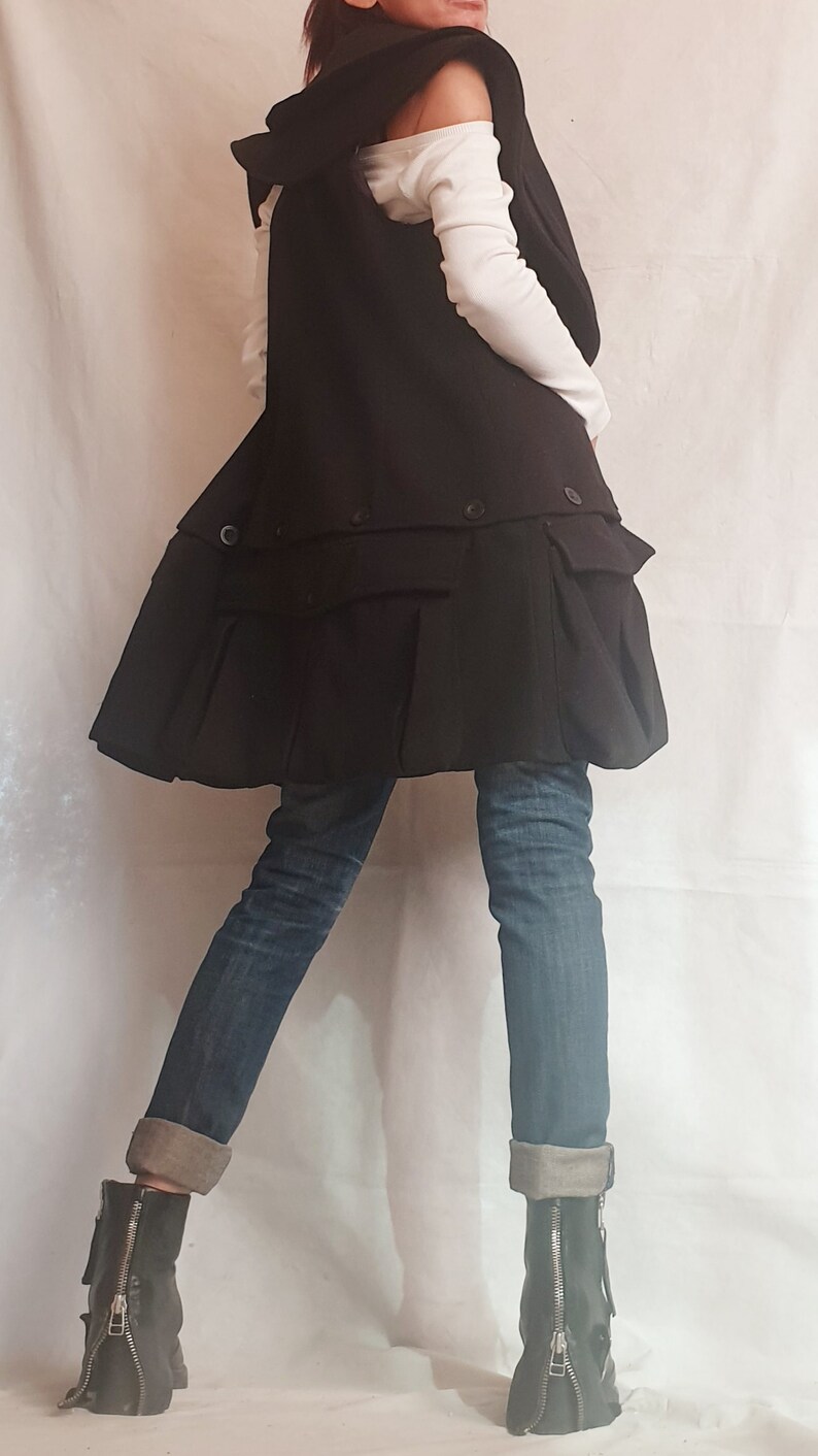 May include: A black vest with a ruffled hem and a white shirt underneath. The vest has a collar and is worn over a white shirt. The person is wearing blue jeans and black boots.