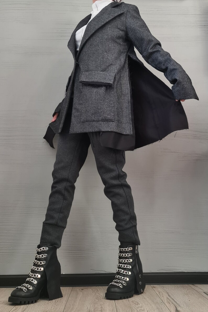 K&ouml;nnte beinhalten: Ein anthrazitfarbener Blazer mit geschlitztem Seitenteil und schwarzem Innenfutter, kombiniert mit einer passenden anthrazitfarbenen, schmal zulaufenden Hose und schwarzen Stiefeletten mit silbernen Ketten und Profilsohle &uuml;ber einem wei&szlig;en Oberteil.
