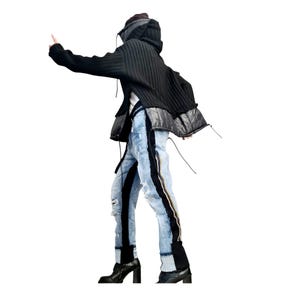 May include: Black hooded sweater with a quilted panel and distressed light blue jeans with black side stripes and a zipper detail. The jeans have ripped sections. The person is wearing black heeled boots.