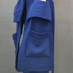 May include: A long, sleeveless royal blue vest with raw, frayed edges and large patch pockets, worn over a white ribbed long-sleeve top and matching royal blue wide-leg trousers with an elasticized waistband and visible seam detailing.