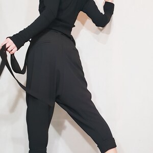 May include: Black off-the-shoulder top with long sleeves and matching black harem pants. The pants have a relaxed fit and cuffed ankles. The outfit is paired with black ankle boots. A stylish and modern ensemble.