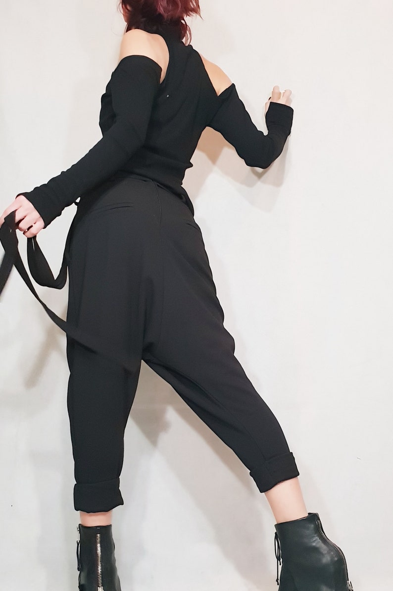 May include: Black off-the-shoulder top with long sleeves and matching black harem pants. The pants have a relaxed fit and cuffed ankles. The outfit is paired with black ankle boots. A stylish and modern ensemble.