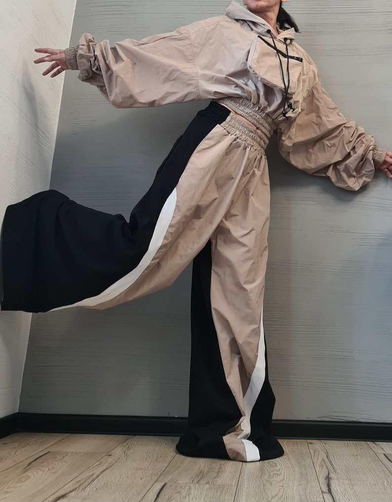 May include: A beige cropped hooded jacket with long sleeves, elastic cuffs, and a front pocket with black drawstrings, paired with wide-leg trousers featuring a color-blocked design in black, beige, and white with a high elasticized waistband.