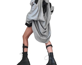 May include: A light gray oversized jacket with black accents and a draped design. The jacket is paired with black platform boots and leg straps, creating a unique, edgy look. The outfit is set against a white background.