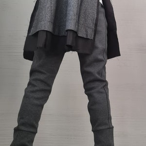 K&ouml;nnte beinhalten: Ein anthrazitfarbener Blazer mit strukturierter Oberfl&auml;che und schwarzen Seiteneins&auml;tzen, kombiniert mit einer passenden, eng anliegenden anthrazitfarbenen Hose mit B&uuml;ndchen. Schwarze Lederstiefeletten mit silbernen Rei&szlig;verschl&uuml;ssen am R&uuml;cken.