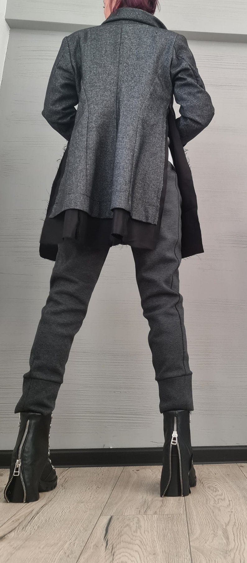 K&ouml;nnte beinhalten: Ein anthrazitfarbener Blazer mit strukturierter Oberfl&auml;che und schwarzen Seiteneins&auml;tzen, kombiniert mit einer passenden, eng anliegenden anthrazitfarbenen Hose mit B&uuml;ndchen. Schwarze Lederstiefeletten mit silbernen Rei&szlig;verschl&uuml;ssen am R&uuml;cken.