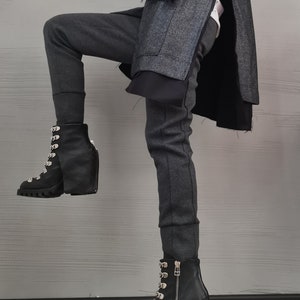 K&ouml;nnte beinhalten: Ein anthrazitfarbener Mantel aus Wollmischgewebe mit Seitenschlitzen, eine dunkelgraue, eng anliegende Hose und schwarze Schn&uuml;rstiefel aus Leder mit silberfarbenen Metallbeschl&auml;gen, einer dicken Profilsohle, einem Rei&szlig;verschluss und drei Nieten.