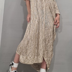 May include: A loose-fitting, beige and white speckled knit dress with short sleeves, an asymmetrical hemline, and a wide neckline. The dress is paired with white platform sandals featuring black buckle straps and a black and white speckled sole.