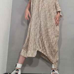 May include: A loose-fitting, beige and white heathered knit tunic dress with an asymmetrical hemline and short sleeves. The garment is paired with white platform sandals featuring black buckle straps and a black and white marbled sole design.