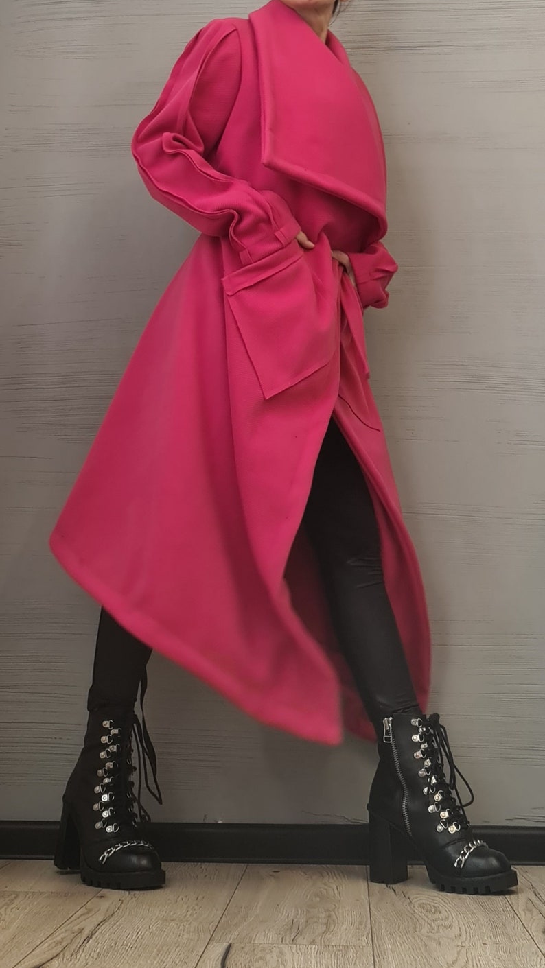 K&ouml;nnte beinhalten: Ein leuchtend pinkfarbener langer Mantel mit breitem Kragen, strukturierten Schultern und gro&szlig;en aufgesetzten Taschen. Der Mantel wird mit einer schwarzen Leggings und schwarzen Schn&uuml;rstiefeletten aus Leder mit silberfarbenen Details kombiniert.