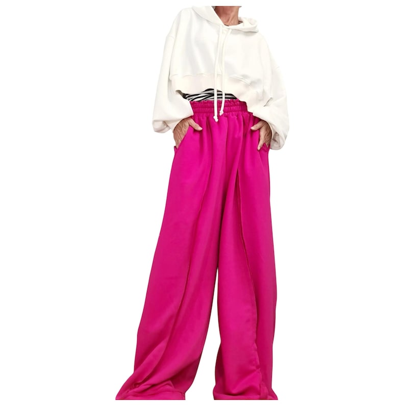May include: A fashion ensemble featuring a white hooded sweatshirt and vibrant fuchsia wide-leg pants. The pants have a high waist and a flowing, pleated design. The outfit is styled with a black and white striped top peeking out from under the sweatshirt.