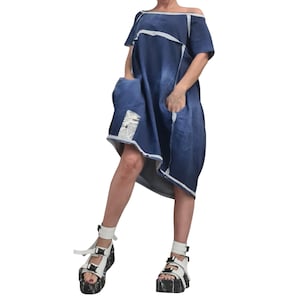 May include: A dark blue denim dress with an off-the-shoulder neckline and short sleeves. The dress has white trim and a pocket with a newspaper print detail. The model is wearing white platform sandals.