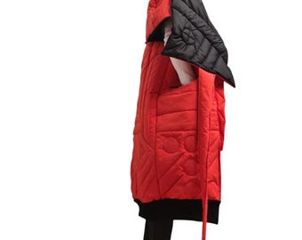 May include: A long, quilted red coat with a black hood and accents. The coat features a unique design with circular patterns and a long, black strap. The hood is black and quilted. The coat is worn over black pants.