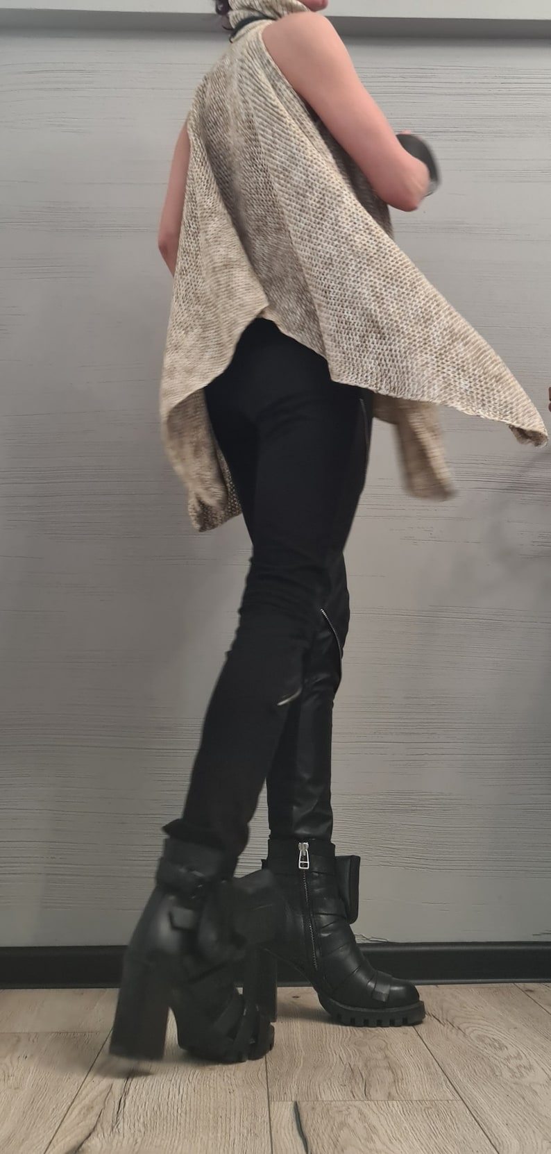 May include: A sleeveless beige knit top with a high collar, paired with black fitted trousers featuring side zippers and black leather-look ankle boots with thick block heels, multiple straps, and silver-toned metal buckles and side zippers.
