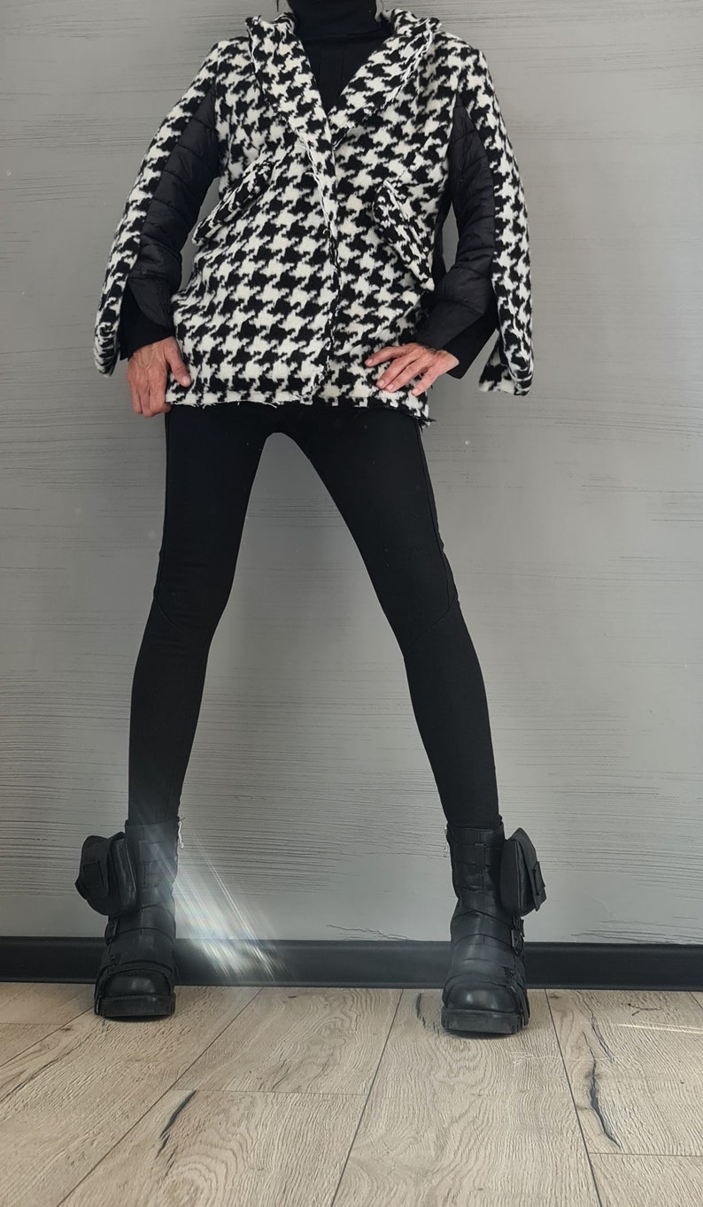 May include: A black and white houndstooth patterned jacket with black quilted sleeves and a high collar, paired with solid black leggings and black leather combat boots featuring side pockets and buckle straps over a black turtleneck sweater.