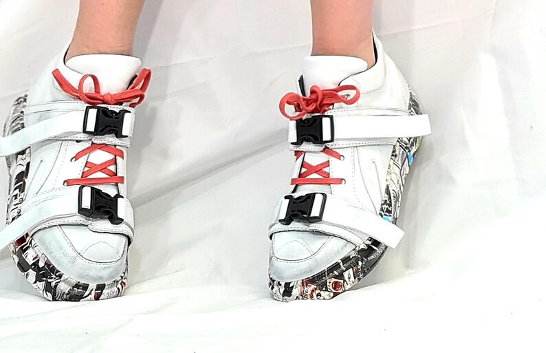 Pu&ograve; includere: Sneakers alte bianche con fibbie nere, lacci color corallo e suola fantasia. Le sneakers hanno cinturini bianchi e un design unico, adatte a persone alla moda.