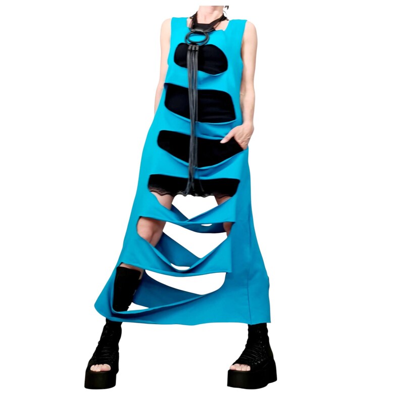 May include: A sleeveless, turquoise dress with large cut-out sections. The dress features black panels and a black leather necklace. The model is wearing black platform boots.
