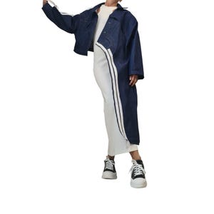 May include: A dark blue denim jacket with white stripes on the sleeves and a matching white stripe down the side of a white dress. The outfit is paired with black and white sneakers.
