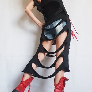 May include: A black sleeveless dress with large cutouts and a distressed design. The dress is paired with denim shorts and red leather boots. The boots have a zipper and a black sole.