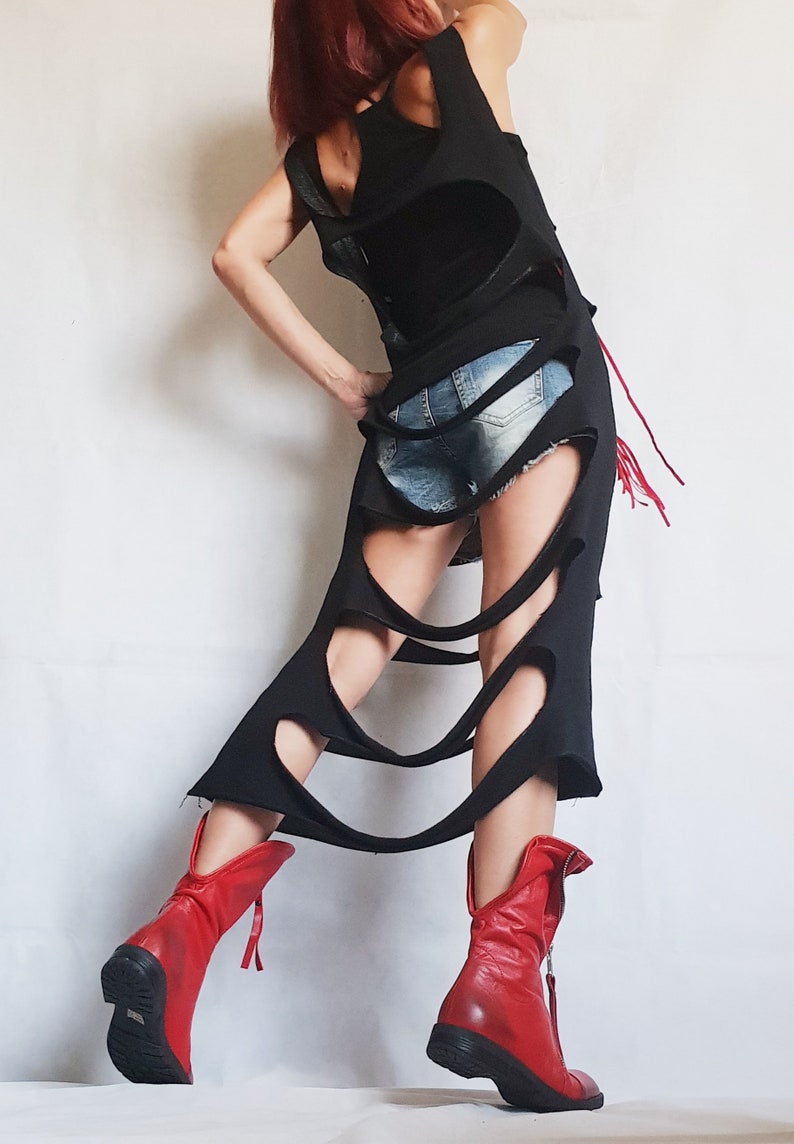May include: A black sleeveless dress with large cutouts and a distressed design. The dress is paired with denim shorts and red leather boots. The boots have a zipper and a black sole.