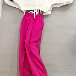 May include: A white cropped hoodie with long sleeves and a drawstring. The sleeves have a black and white striped detail. Paired with bright pink wide-leg sweatpants. A black and white striped shirt is visible underneath the hoodie.