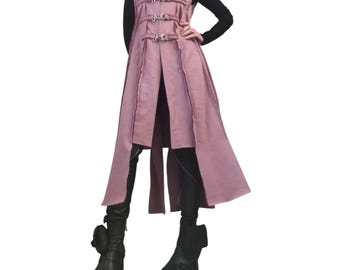 May include: A sleeveless, dusty rose-colored vest with a high collar and decorative metal clasps. The vest has a long, flowing design with vertical seams and is paired with black clothing and boots.