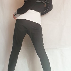 Op de afbeelding: Een zwart kort jasje met zichtbare grijze naden en grijze mouwboorden, gedragen over een wit topje met een zwarte, nauwsluitende broek. De outfit wordt gecompleteerd door zwarte enkellaarsjes met gespen en ritsen, gezien vanaf de achterkant.